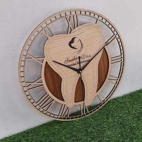 A stylish wall clock designed for a dental office, featuring a large wooden tooth at the center. The clock has an elegant Roman numeral frame and the CUSTOM text displayed prominently on the tooth. The clock is placed on green floor front of white wall