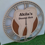 A stylish wall clock designed for a dental office, featuring a large wooden tooth at the center. The clock has an elegant Roman numeral frame and the CUSTOM text displayed prominently on the tooth. The clock is placed on green floor front of white wal